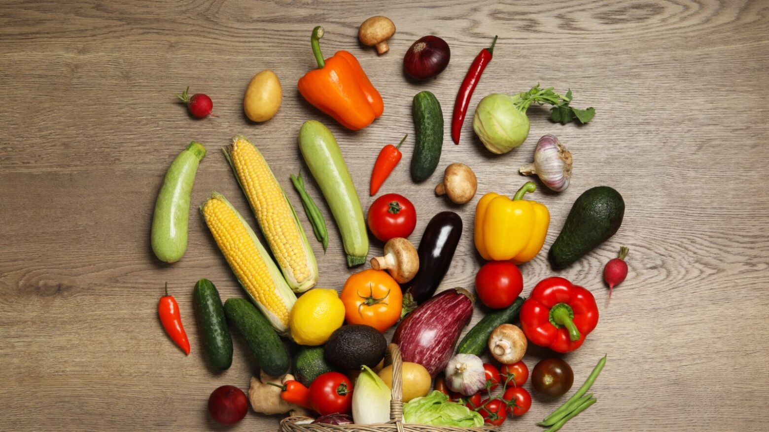 View from above of an assortment of fruits and vegetables spilled out from a basket onto a table.