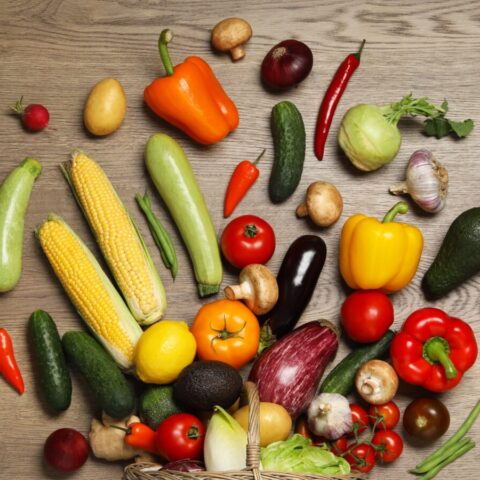 View from above of an assortment of fruits and vegetables spilled out from a basket onto a table.