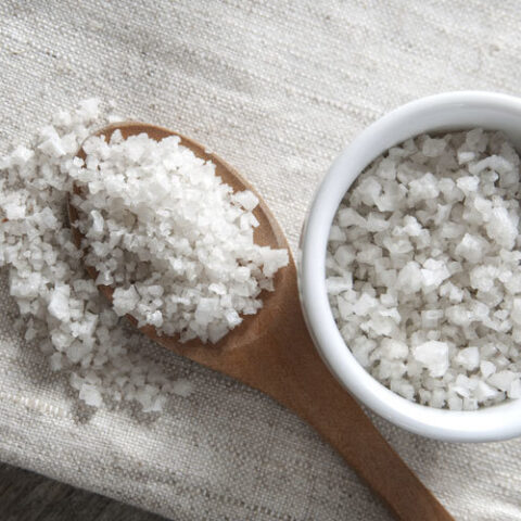 Celtic sea salt in a bowl and on a wooden spoon on a table cloth.