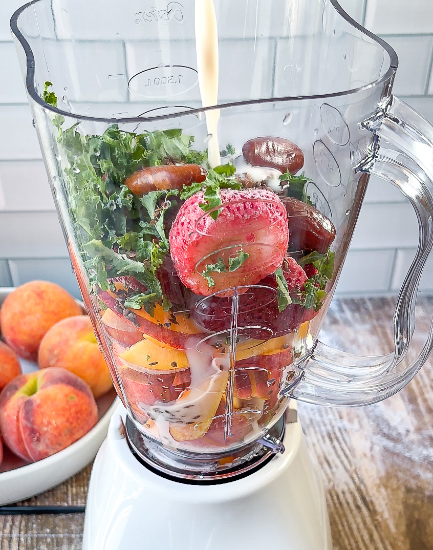 Milk pouring in blender along with the rest of the ingredients. Peach in background