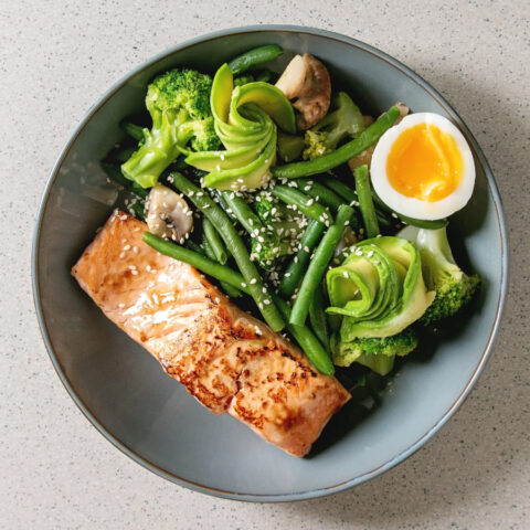 A keto-friendly bowl of salmon, a hard-boiled egg, green beans, avocado, and broccoli