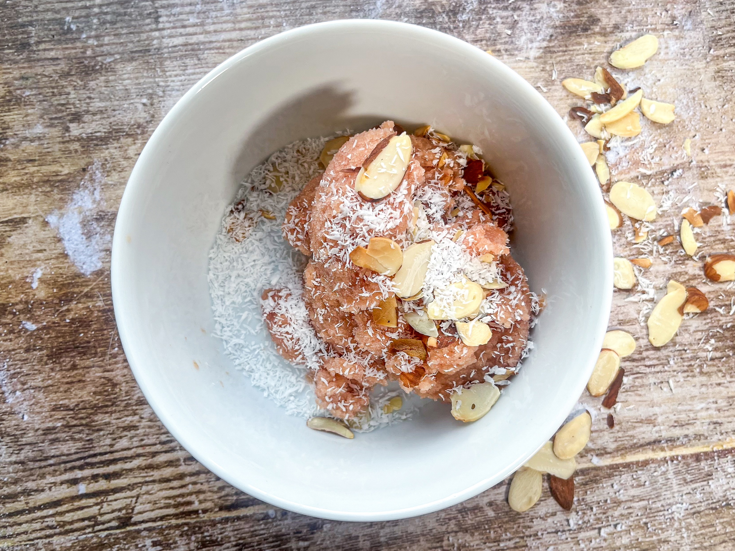 Peach sherbet in a bowl with almonds and shredded coconut