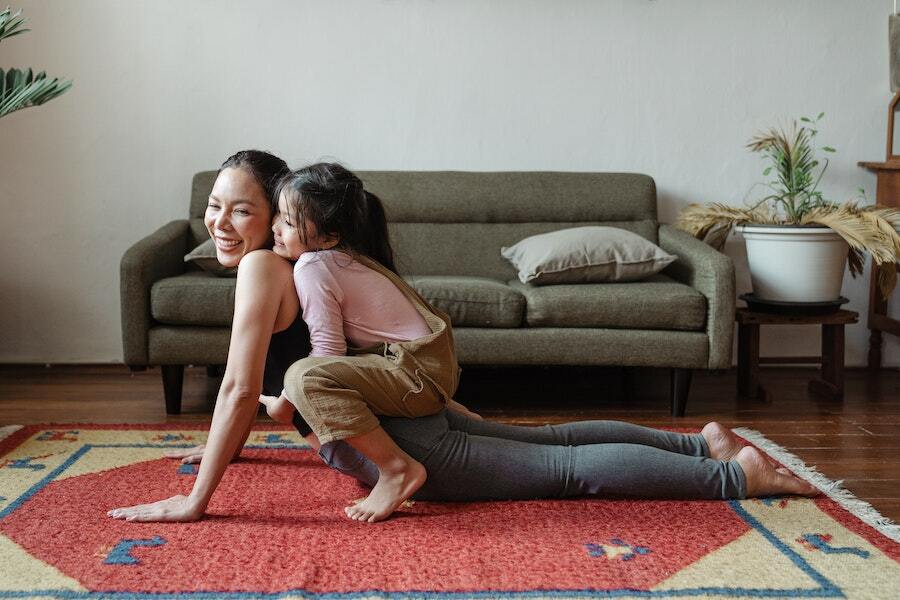 A woman smiles while doing a yoga pose with her young child on her back.