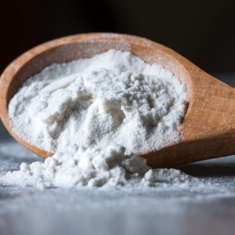 A wooden spoon spills tapioca flour onto a table.