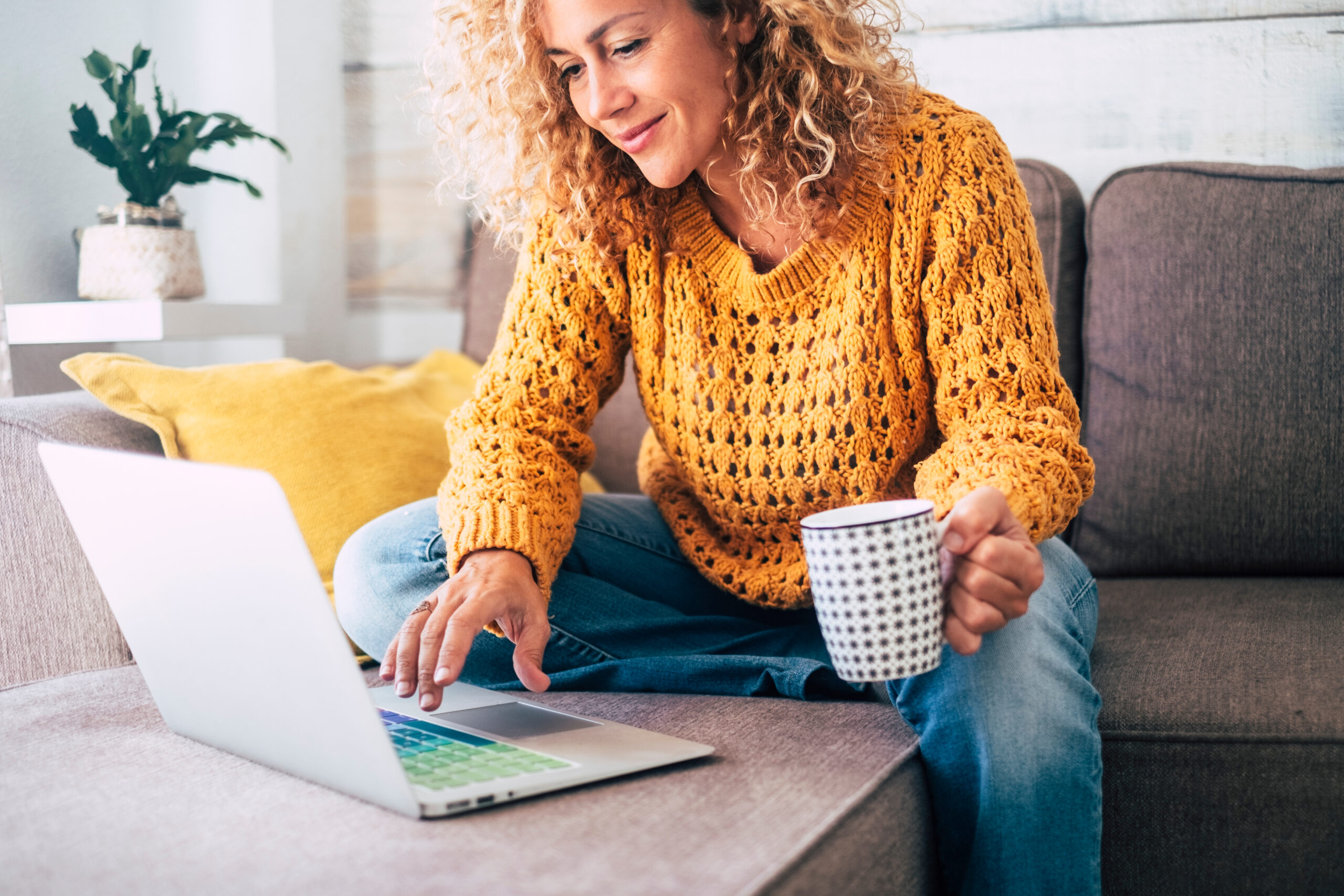 Beautiful woman in orange sweater sits on couch and visits The Paleo Diet website on her laptop.