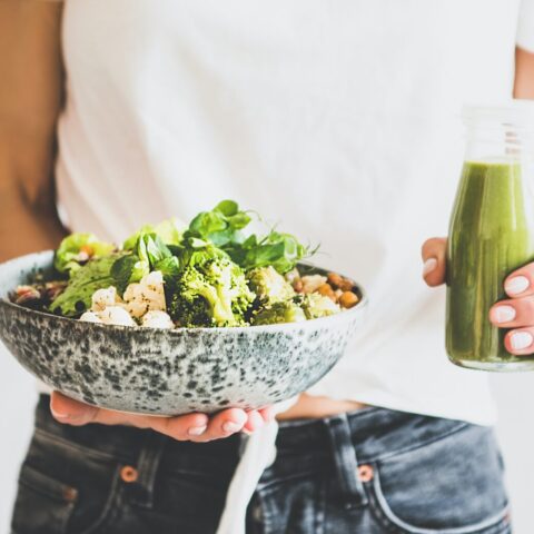 A person holding a bowl of salad and a bottle of green dressing.