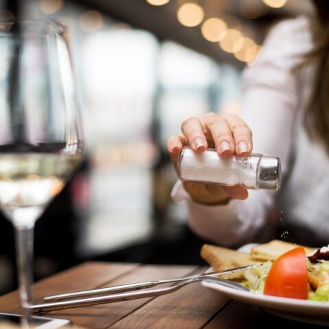 Is salt Paleo? A woman adds salt to a dish at a restaurant.