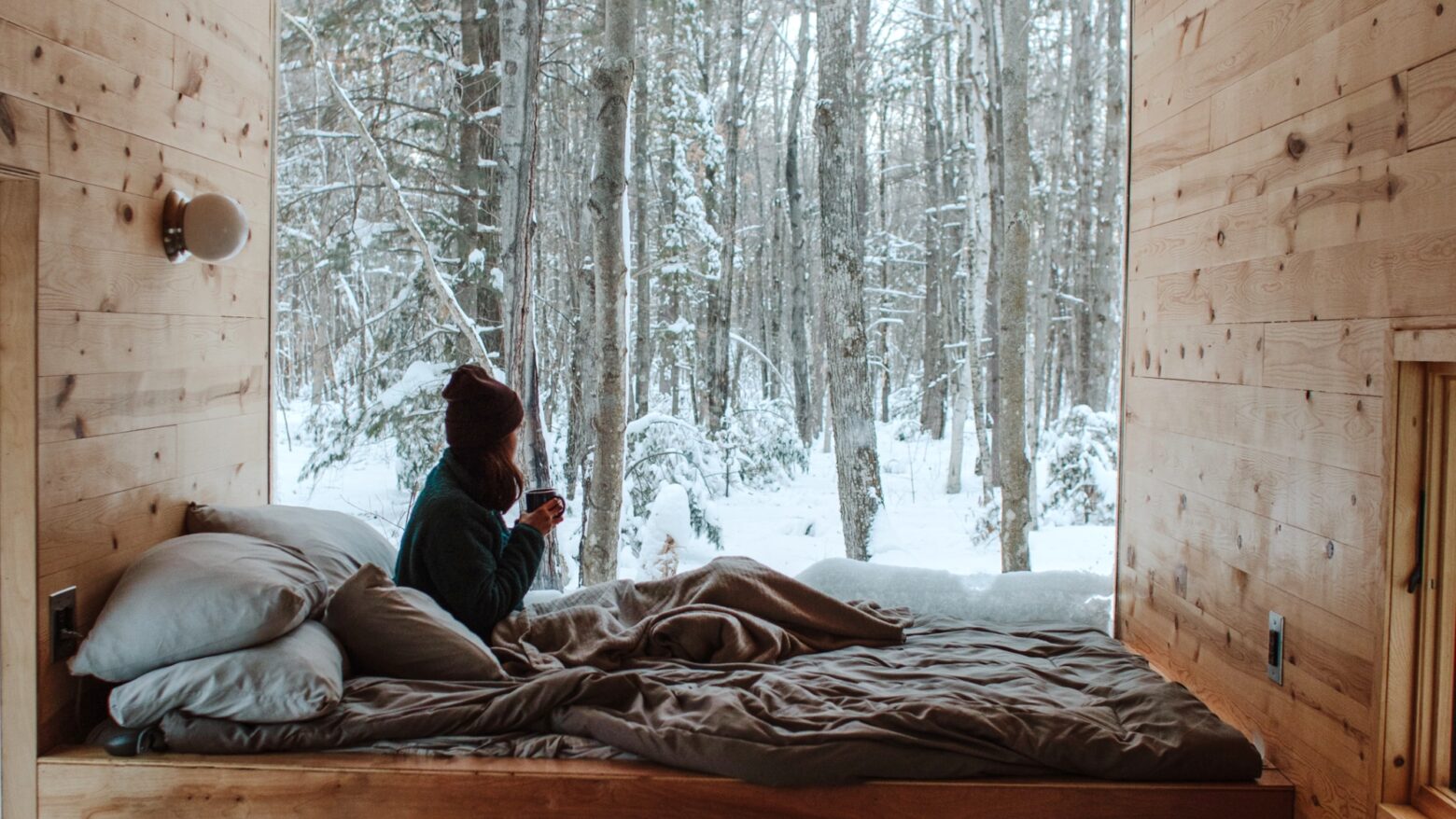 Woman looking out a large bedroom window to a winter landscape