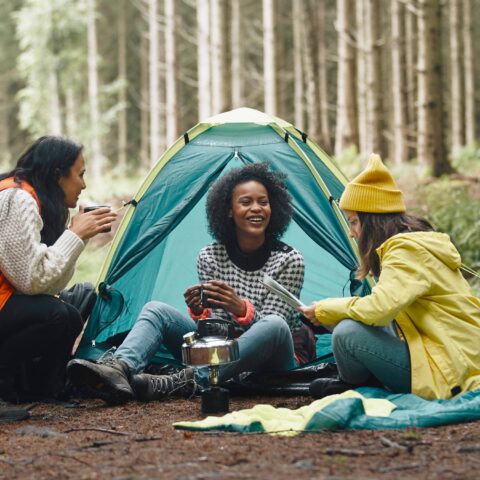 Three women gather around a tent while camping