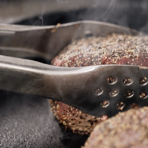 A peppercorn-crusted filet mignon sears in a cast iron skillet.